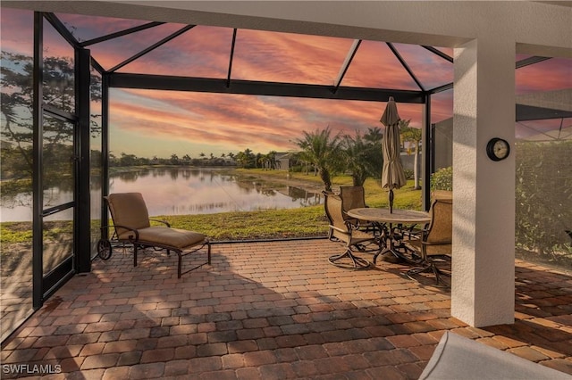 patio terrace at dusk featuring a water view and glass enclosure