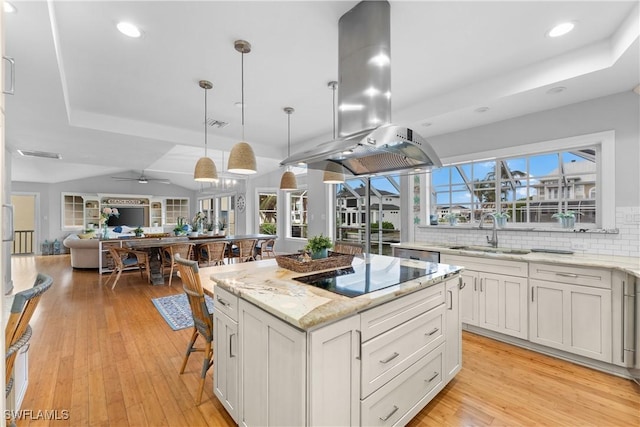 kitchen featuring island exhaust hood, light stone counters, sink, decorative light fixtures, and a center island