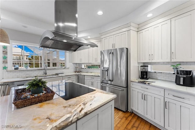 kitchen featuring island exhaust hood, decorative backsplash, black electric stovetop, sink, and stainless steel fridge with ice dispenser