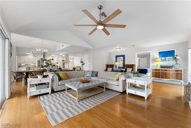 living room with ceiling fan with notable chandelier, vaulted ceiling, and light hardwood / wood-style flooring