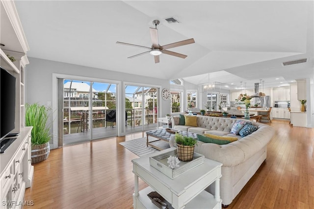 living room featuring ceiling fan with notable chandelier, vaulted ceiling, and light hardwood / wood-style flooring