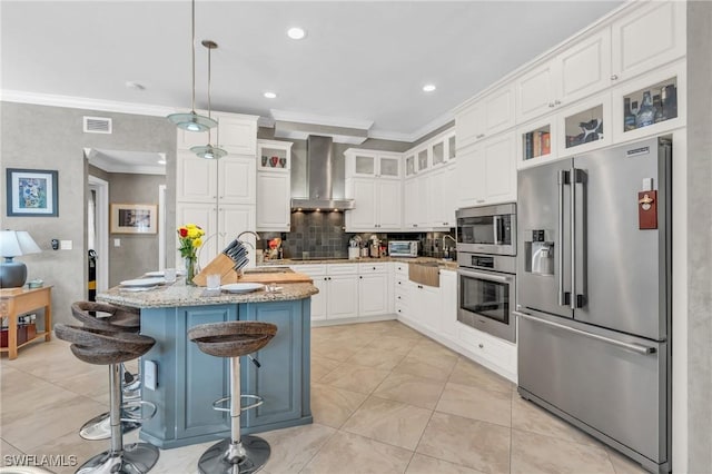 kitchen featuring light stone countertops, pendant lighting, appliances with stainless steel finishes, wall chimney exhaust hood, and an island with sink