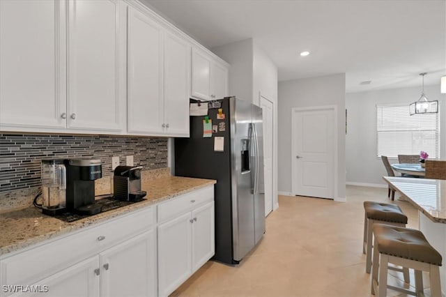 kitchen featuring white cabinets, light stone counters, and stainless steel refrigerator with ice dispenser