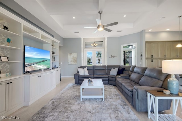 living room featuring a raised ceiling, built in features, french doors, and ceiling fan with notable chandelier