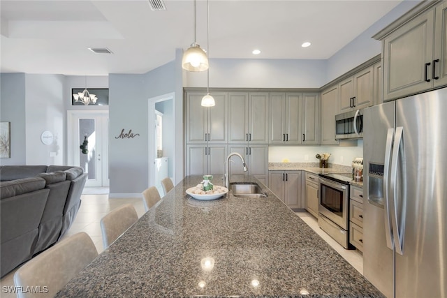 kitchen featuring sink, dark stone counters, decorative light fixtures, a breakfast bar area, and appliances with stainless steel finishes