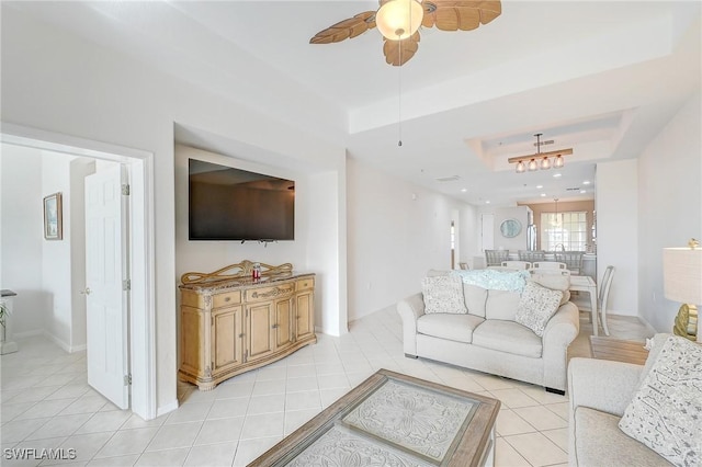 living room with a tray ceiling, ceiling fan, and light tile patterned flooring