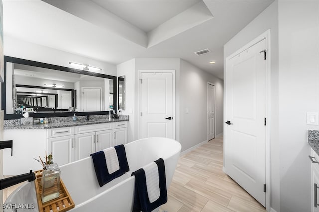 bathroom with hardwood / wood-style flooring, vanity, a raised ceiling, and a bathtub