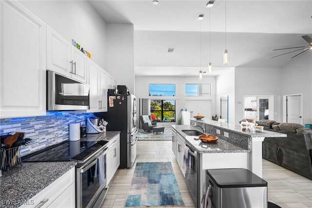 kitchen with appliances with stainless steel finishes, white cabinetry, sink, hanging light fixtures, and a kitchen island with sink