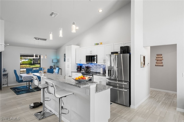 kitchen featuring pendant lighting, white cabinets, a kitchen breakfast bar, light stone counters, and stainless steel appliances