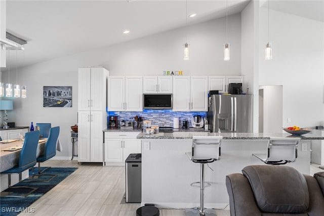 kitchen with hanging light fixtures, a kitchen breakfast bar, stainless steel appliances, light stone countertops, and white cabinets