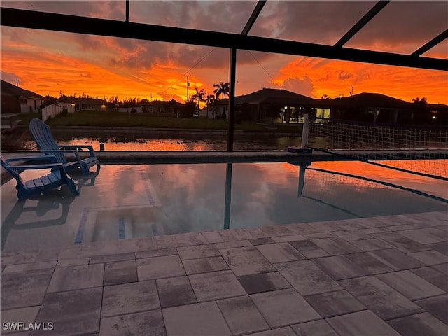 pool at dusk with glass enclosure and a patio area