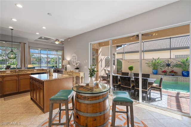 kitchen with sink, a center island, hanging light fixtures, ceiling fan, and light stone countertops