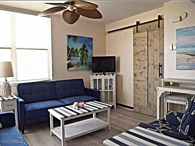 living room with a barn door, ceiling fan, and wood-type flooring