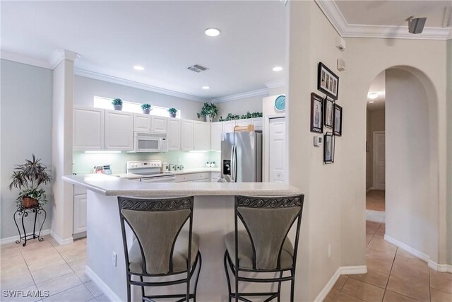 kitchen featuring a kitchen bar, white appliances, crown molding, light tile patterned floors, and white cabinets