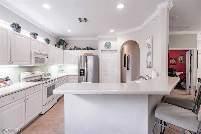 kitchen with light tile patterned floors, white appliances, white cabinetry, and a breakfast bar area