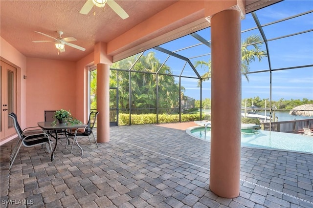 view of patio / terrace with ceiling fan, a water view, and glass enclosure