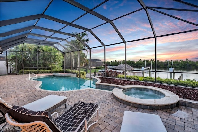 pool at dusk featuring a lanai, a patio area, an in ground hot tub, and a water view