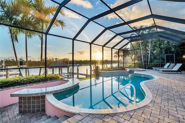 pool at dusk featuring a lanai, a patio area, and a water view