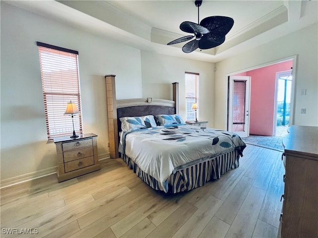 bedroom with a tray ceiling, ceiling fan, light hardwood / wood-style floors, and access to outside