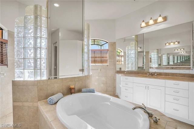 bathroom with tile patterned flooring, a relaxing tiled tub, tile walls, and vanity