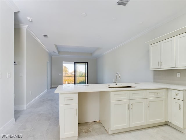 kitchen featuring white cabinets, a raised ceiling, crown molding, sink, and kitchen peninsula