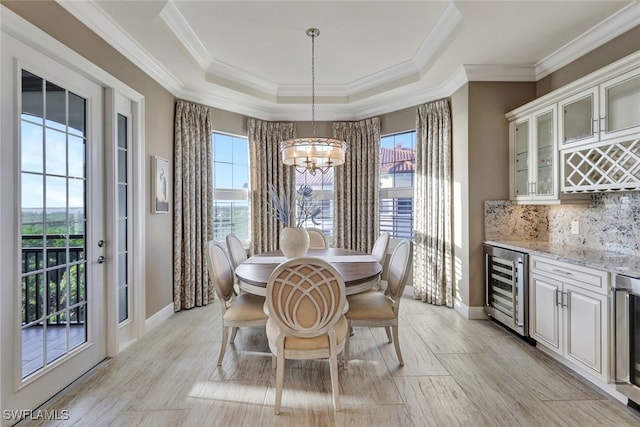 dining space with a tray ceiling, wine cooler, plenty of natural light, and a notable chandelier