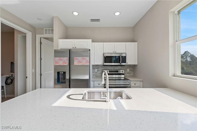 kitchen with white cabinetry, appliances with stainless steel finishes, light stone countertops, and plenty of natural light