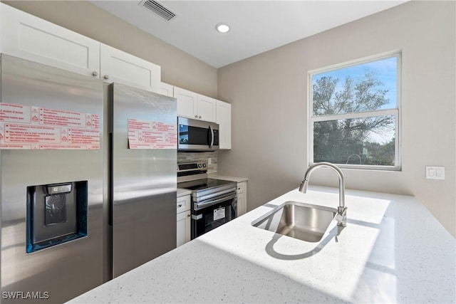 kitchen with light stone countertops, appliances with stainless steel finishes, sink, and white cabinets