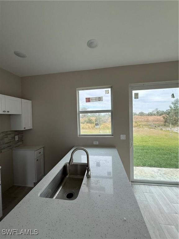 kitchen featuring white cabinetry, a wealth of natural light, light stone countertops, and sink