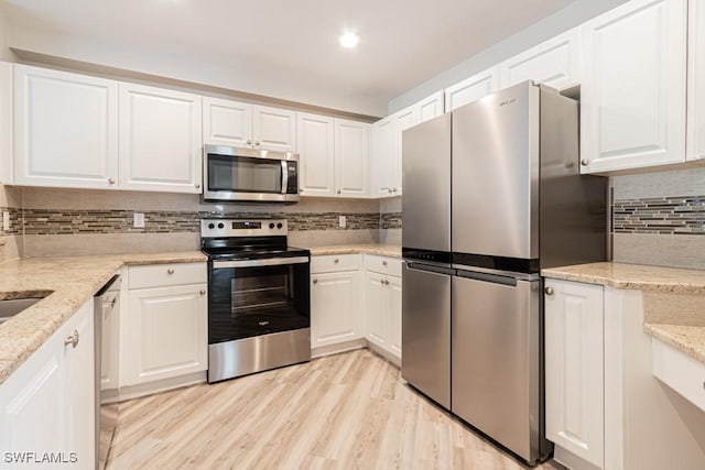 kitchen featuring backsplash, white cabinets, light stone countertops, appliances with stainless steel finishes, and light hardwood / wood-style floors