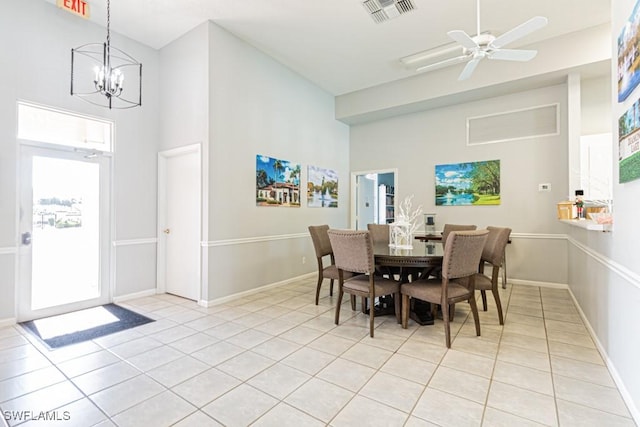 dining area with light tile patterned floors, ceiling fan with notable chandelier, and a high ceiling