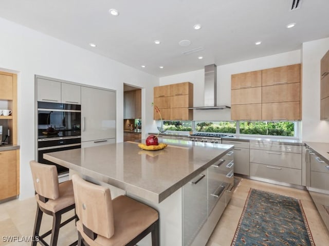 kitchen featuring wall chimney exhaust hood, a large island, modern cabinets, and a breakfast bar