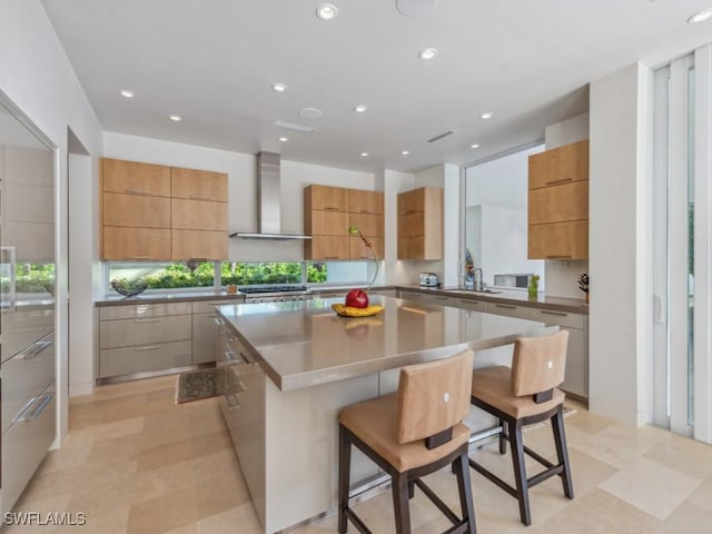 kitchen with wall chimney exhaust hood, modern cabinets, a breakfast bar area, a center island, and recessed lighting