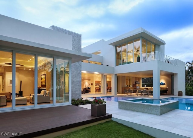 rear view of house featuring outdoor dining space, a pool with connected hot tub, a patio, and a balcony