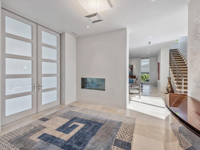 entryway featuring recessed lighting, french doors, a glass covered fireplace, and stairs