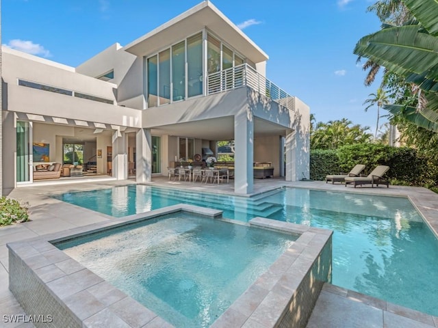 back of house featuring a patio, a balcony, a pool with connected hot tub, and stucco siding