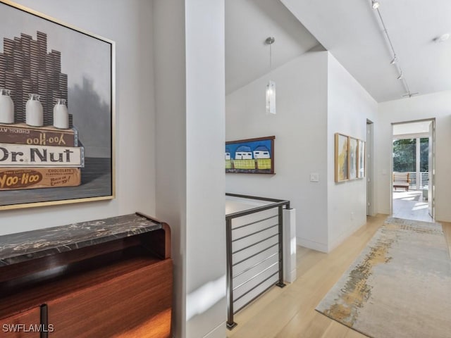 hall with baseboards, light wood-type flooring, an upstairs landing, and track lighting