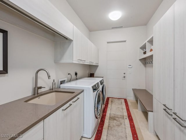 laundry area with washing machine and dryer, cabinet space, a sink, and visible vents