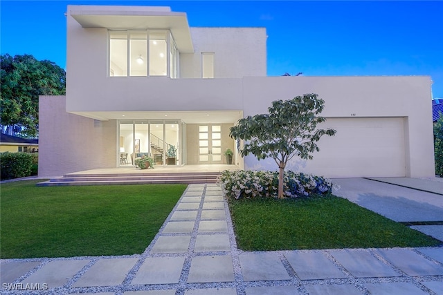 contemporary home with a front yard, concrete driveway, an attached garage, and stucco siding