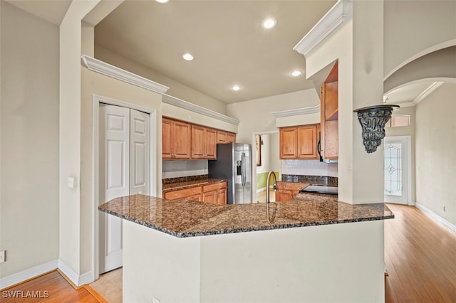 kitchen featuring sink, stainless steel fridge with ice dispenser, kitchen peninsula, dark stone counters, and light hardwood / wood-style floors