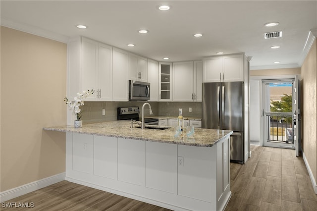 kitchen with hardwood / wood-style floors, white cabinets, ornamental molding, kitchen peninsula, and stainless steel appliances