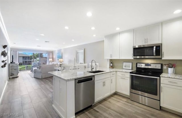 kitchen with kitchen peninsula, sink, light stone countertops, appliances with stainless steel finishes, and white cabinetry