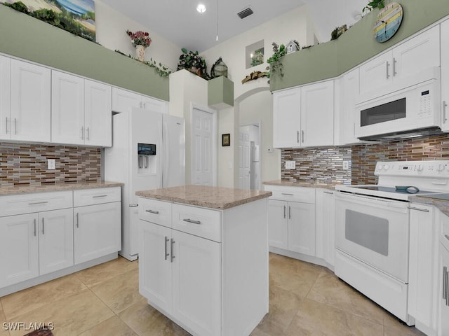 kitchen with white cabinets, a towering ceiling, white appliances, and tasteful backsplash