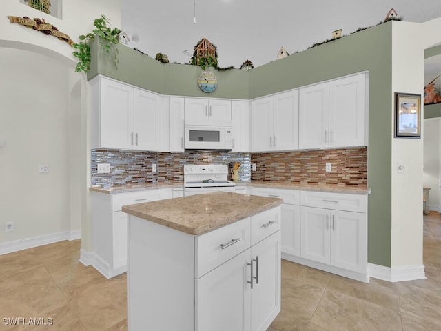 kitchen with a center island, white appliances, backsplash, light tile patterned flooring, and white cabinetry