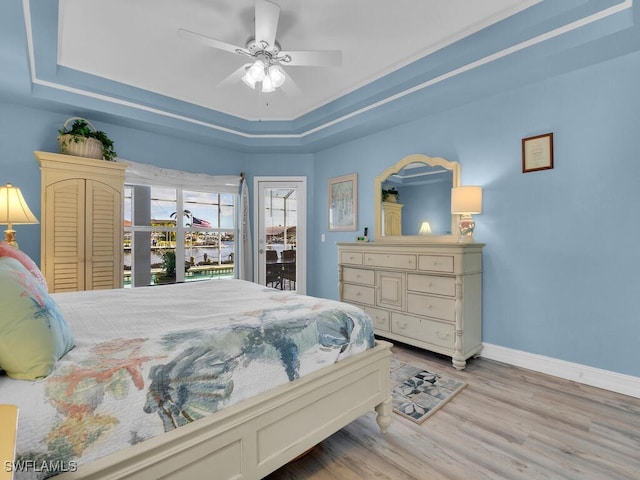 bedroom with ceiling fan, light hardwood / wood-style flooring, and a tray ceiling