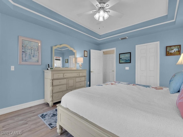 bedroom featuring ceiling fan, a raised ceiling, light wood-type flooring, and a closet