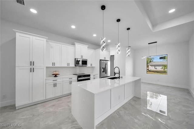 kitchen with white cabinets, appliances with stainless steel finishes, a center island with sink, and sink