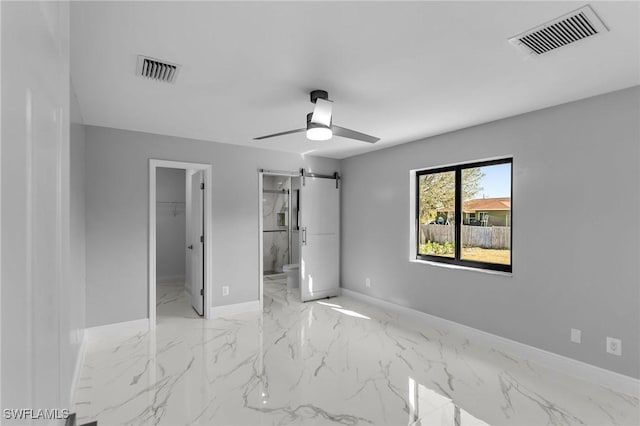 unfurnished bedroom featuring ensuite bathroom, ceiling fan, a barn door, a spacious closet, and a closet