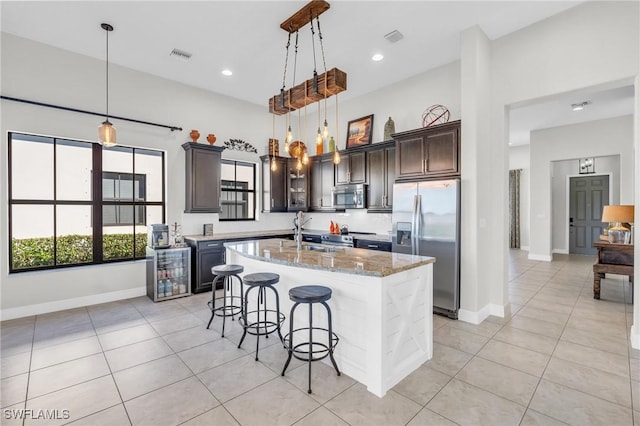 kitchen with appliances with stainless steel finishes, pendant lighting, light stone counters, and a center island with sink