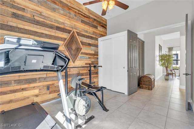 workout room featuring ceiling fan, light tile patterned floors, and wood walls